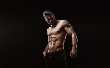 Muscular model sports young man on dark background. Fashion portrait of strong brutal guy with a modern trendy hairstyle. Sexy torso. Male flexing his muscles.