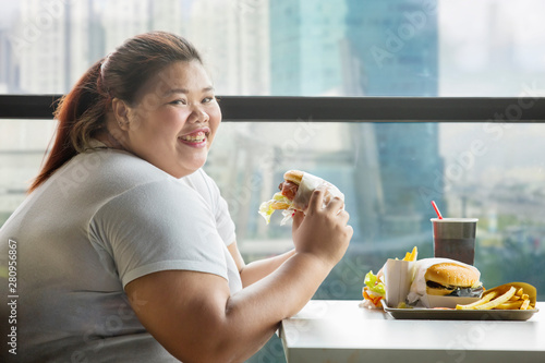Fotomural Happy fat woman eats a hamburger in restaurant