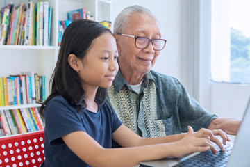 Wall Mural - Little girl learns to use a laptop with her grandfather