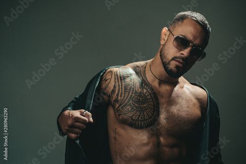 Fashionable tattoo. Muscular hispanic man with tattoo on chest. Strong latino man with tattoo on skin. Tattooed guy with muscle torso and tattoo