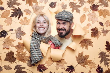 Wall Mural - Bearded man in cap and blond girl with scarf are happy with autumn sales. Romantic couple wearing pullover on autumn leaves background. Autumn mood and weather are warm and sunny and rain is possible.