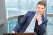 © DragonImages - Young entrepreneur in suit working at table in corner office of skyscraper building