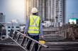 © zephyr_p - Asian maintenance worker man with safety helmet and green vest carrying aluminium step ladder and tool box at construction site. Civil engineering, Architecture builder and building service concepts