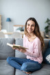 © BestForYou - Young woman sitting on sofa at home and reading a book.