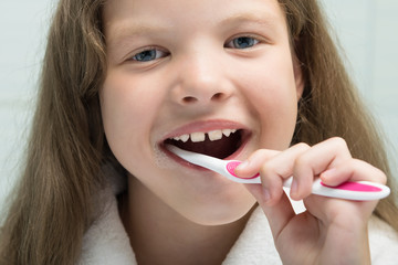 little girl in a white robe smiling brushes her teeth, close-up