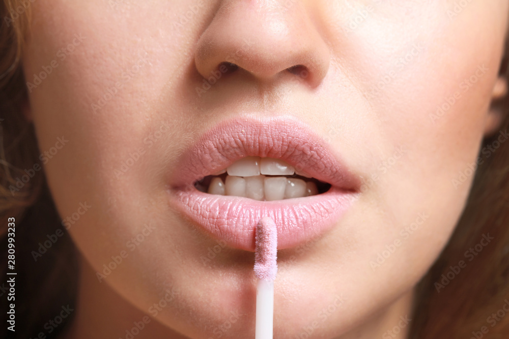 Beautiful young woman applying lipstick, closeup
