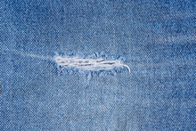 Hole with frayed threads in an old torn blue jeans