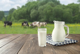 Fresh milk in glass on dark wooden table and blurred landscape with cow on meadow. Healthy eating. Rustic style.