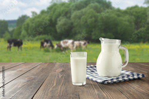 Fotografía Fresh milk in glass on dark wooden table and blurred landscape with cow on meadow