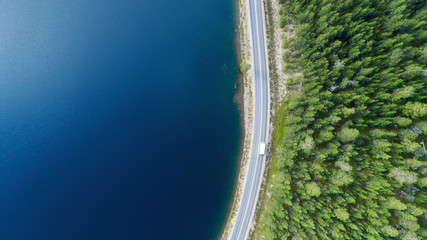 Wall Mural - Aerial view of white caravan car driving on country road in forest near lake with beautiful blue water. Driving a car.