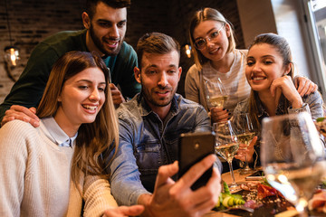 Wall Mural - Group of young friends having fun in restaurant, talking and laughing while dining at table.