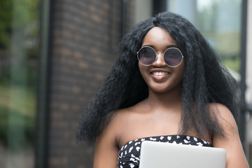 Wall Mural - Cropped portrait of a African american woman business woman in glasses with your laptop while standing  in the city.