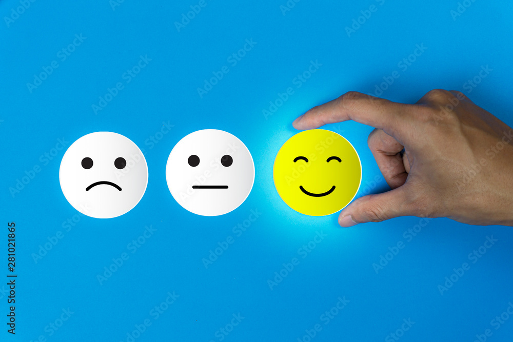 Conceptual the customer responded to the survey. The client using hand choose happy face smile icon on blue background.Depicts that customer is very satisfied. Service experience satisfaction concept. - obrazy, fototapety, plakaty 
