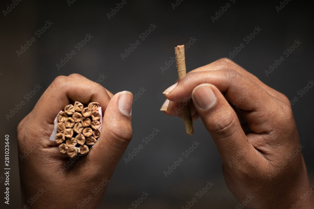 Closeup of Hands holding Beedi or bidi cigarette in dark room. Stock Photo 