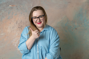 Wall Mural - Portrait of attractive plus size in glasses woman having emotions positive, joy and surprise isolated over colored background. Concept of emotions. Raised up thumb.