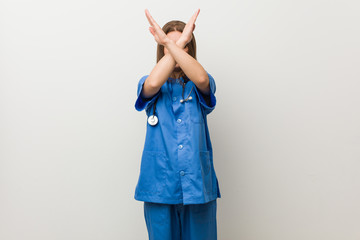 Wall Mural - Young nurse woman against a white wall keeping two arms crossed, denial concept.