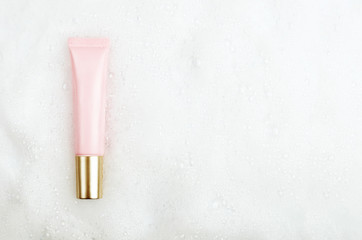 Wall Mural - Pink tube with gel or face cream with a golden cap on a background of white foam with bubbles. Copy space, top view, flat lay.