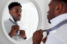 Businessman At Home Tying Necktie In Mirror Before Leaving For Work