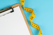 © Nuthawut - Healthy eating plan, diet or fitness planning, blank white paper on clipboard with measuring tape on solid blue background, writing message to set target or goal, menu or message