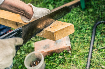 Man in gloves sawing a wooden board with a hand saw