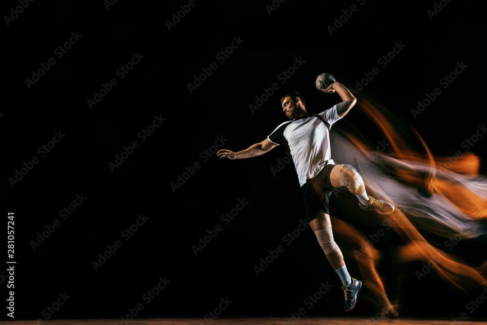 Caucasian young handball player in action and motion in mixed lights over black studio background. Fit male professional sportsman. Concept of sport, movement, energy, dynamic, healthy lifestyle. - obrazy, fototapety, plakaty 