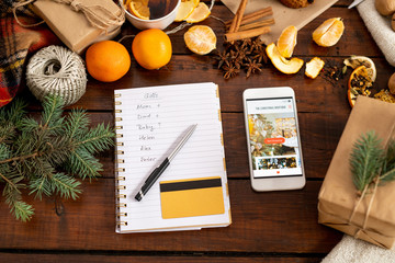 Smartphone with promo, notepad, penand credit card among xmas stuff on table