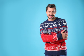 Portrait of happy young man in Christmas sweater on light blue background. Space for text