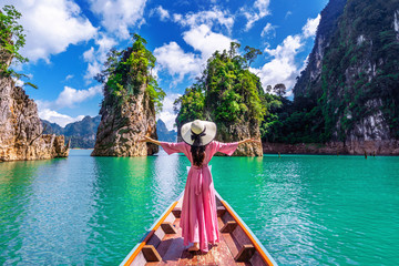 Wall Mural - Beautiful girl standing on the boat and looking to mountains in Ratchaprapha Dam at Khao Sok National Park, Surat Thani Province, Thailand.