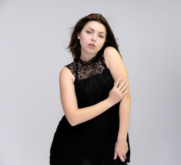 A portrait above the knee of a pretty beautiful fashionable adult brunette girl in a black dress on a white background. Standing right in front of the camera, showing different poses and emotions.