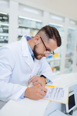 Wall Mural - Attentive young chemist writing prescription for pills