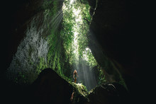 Young Girl Girl Stands Under The Ray Of Light In The Cave  In Bali,  Indonesia. Tukad Cepung Waterfall