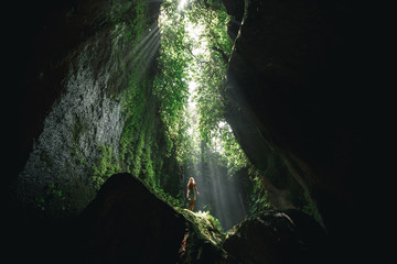 Young girl Girl stands under the ray of light in the cave  in Bali,  indonesia. Tukad Cepung waterfall