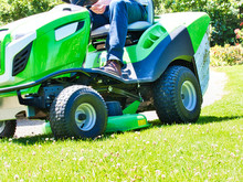 Senior Man Driving A Tractor Lawn Mower In Garden With Flowers
