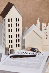 Wall Mural - houses models on white wooden table with contract, keys and coins, real estate concept