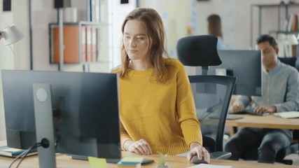 Wall Mural - beautiful and smart red haired female specialist sitting at her desk works on a desktop computer. br