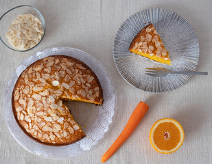 Aerial view of homemade cake with carrots, almonds and orange. Dish with a piece of cake ready to eat