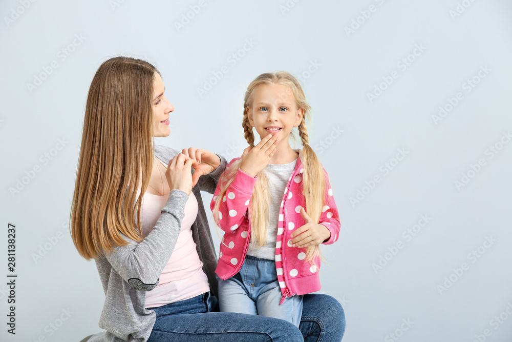 Little deaf mute girl and her mother using sign language on light background
