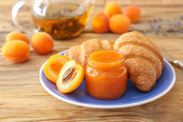 Plate with tasty apricot jam and croissants on wooden table