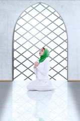 Wall Mural - Asian Muslim woman in veil sitting in pray position while raised hands and praying