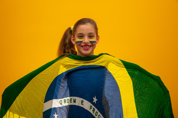 Football supporter, Brazil team. World Cup. Beautiful little girl cheering for her team on yellow background