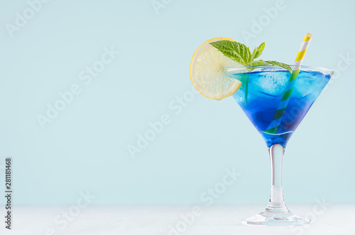 Fotografía Bright summer fresh blue fruit cocktail with blue curacao liquor, ice cubes, lemon slice, green mint in pastel mint color interior on white wood board
