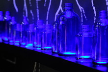 Blue Glass Bottles In Various Size On Shelf With Bottom Lighted. Dark Environment. Perspective