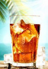 Poster - Table background with ice tea on a wooden table top with beautiful blue sky and ocean and palm tree view.