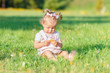 © Igor Butseroga - Cute little girl sits on the green grass, outdoors, summer time, blurred background