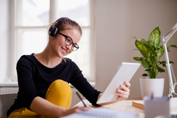 Poster - A young female student sitting at the table, using headphones when studying.