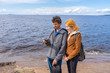 © Tatyana_Andreyeva - Middle aged man and young lady standing on northern lake shore in summer day. Tourists taking pictures on smartphone. Travelling and discovering distant places of Earth. Onega lake, Karelia, Russia