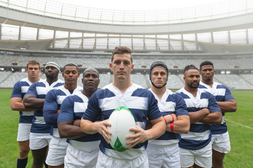 Group of diverse male rugby players standing together with rugby ball in stadium