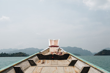 Exotic wooden boat with tropical islands with rocks and blue lake at Cheow Lan Lake, Khao Phang, Ban Ta Khun District, Thailand. Travel, holiday and adventure concept.