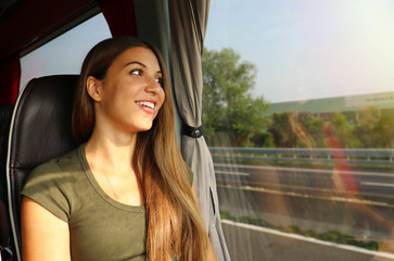 Canvas Print - Young beautiful woman looking through the bus window. Happy bus passenger traveling sitting in a seat and looking through the window.