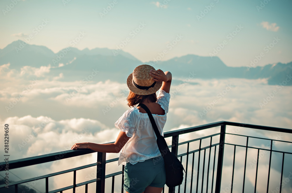 the girl in a straw hat costs at top of the mountain and looks afar at ...